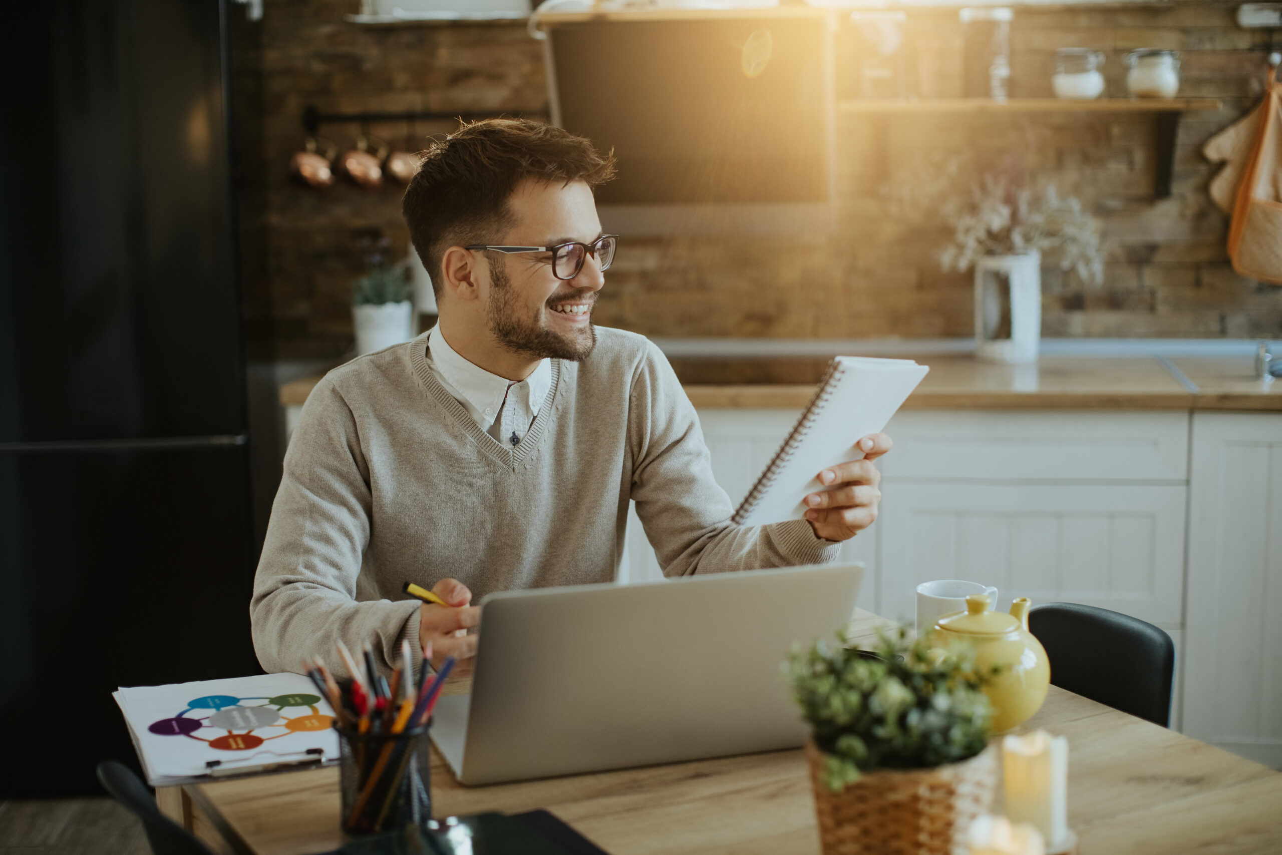 Young happy businessman using laptop and reading notes while working at home.